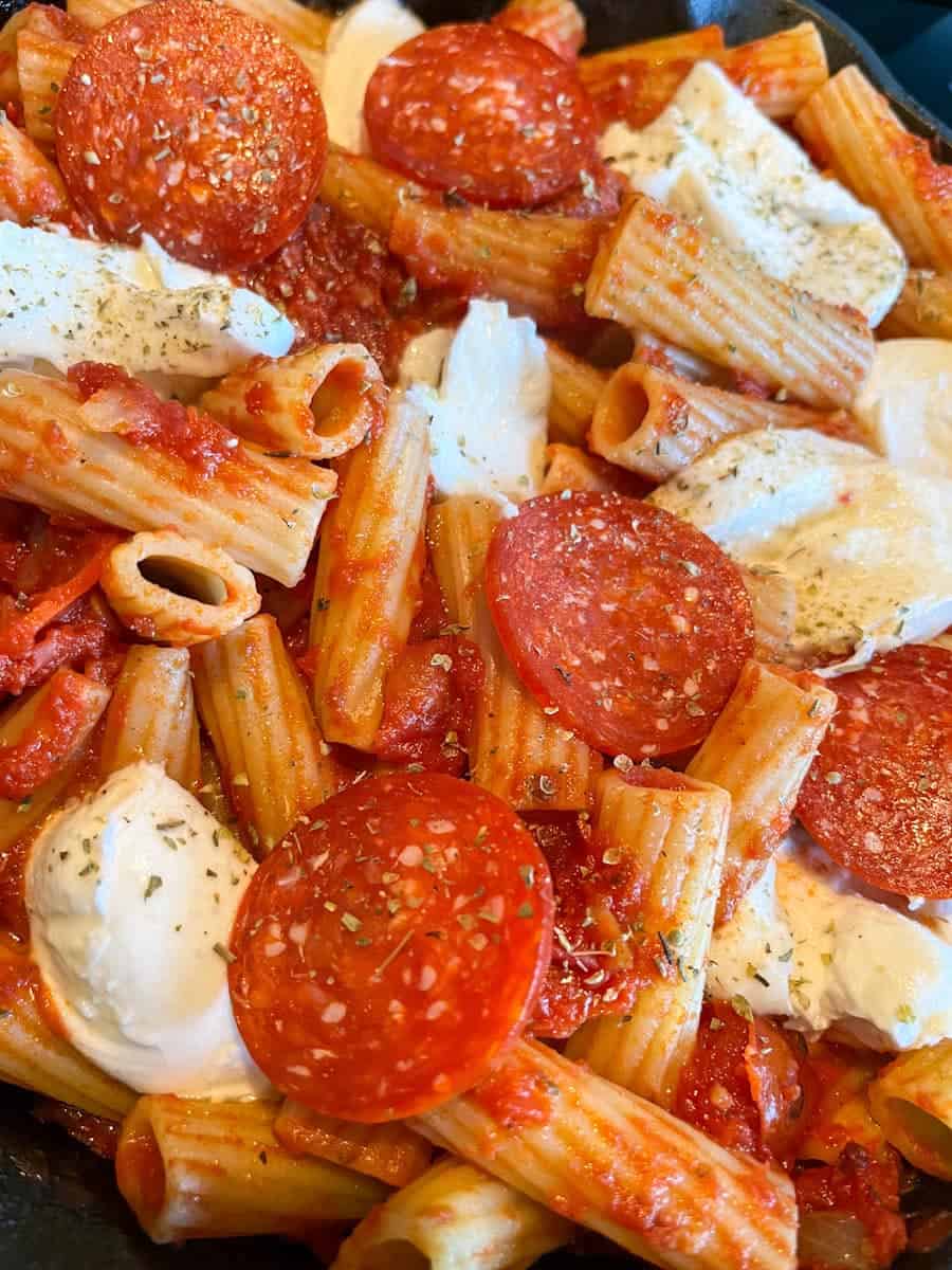 a pan of rigatoni pasta in tomato sauce topped with pepperoni slices and mozarella cheese.
