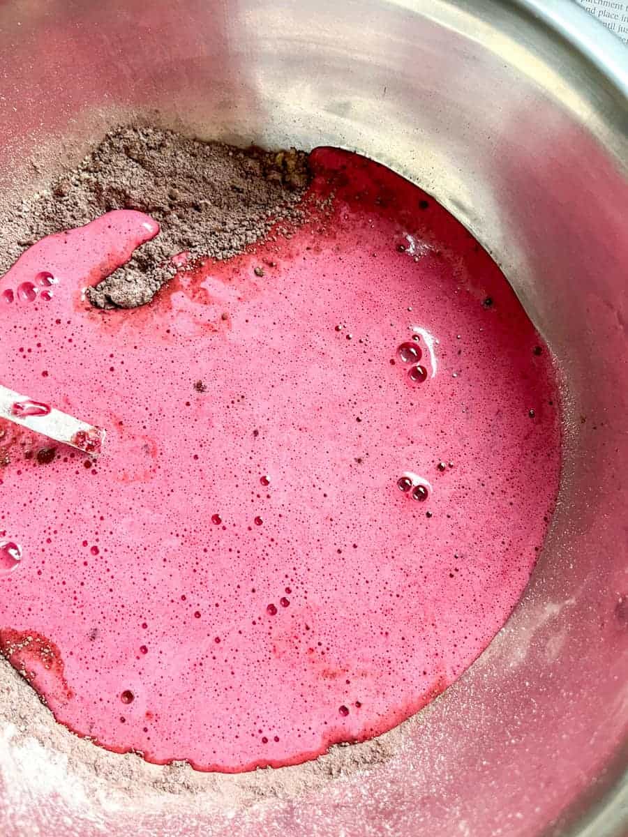 pureed beetroot, sugar and eggs being stirred into a silver bowl of cocoa powder and flour.