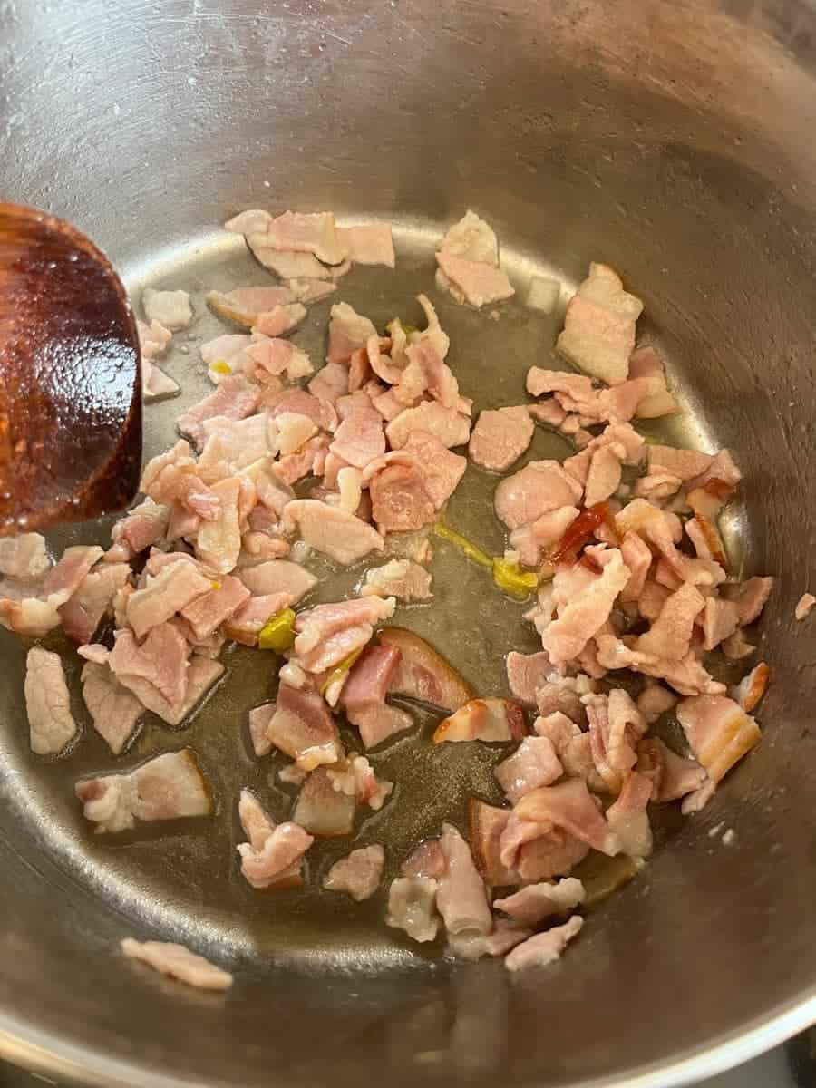bacon pieces cooking in a silver saucepan.