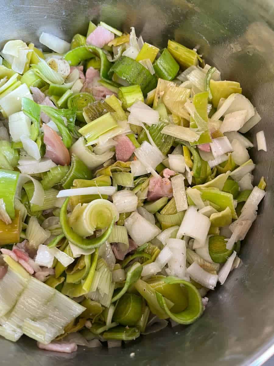 sliced leeks, bacon and onion in a silver saucepan.