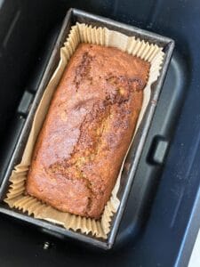 a baked banana bread in a loaf tin inside an air fryer.