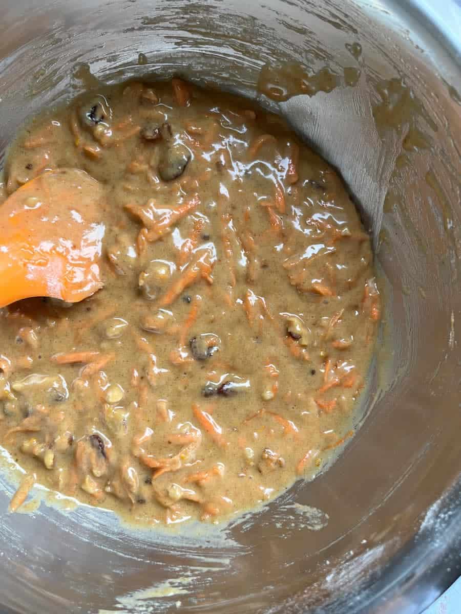 a silver bowl of carrot cake batter with an orange spatula.