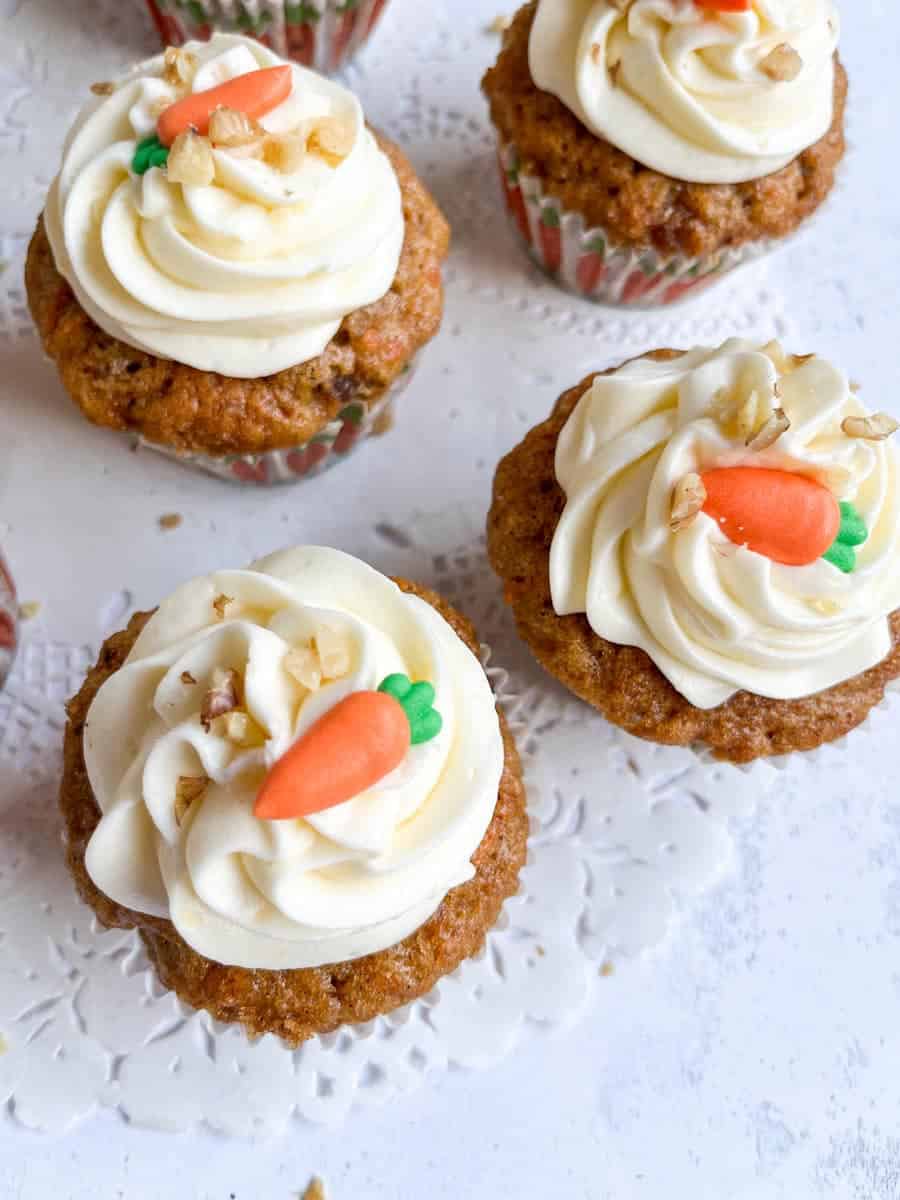 carrot cake cupcakes topped with a cream cheese icing swirl, chopped walnuts and a mini fondant carrot.