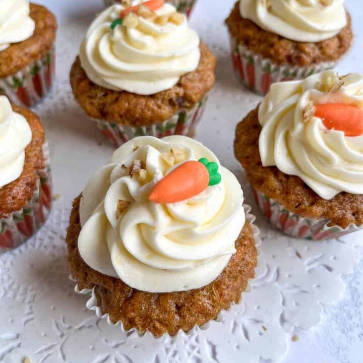seven carrot cake cupcakes decorated with a cream cheese icing swirl, chopped walnuts and a mini fondant carrot.