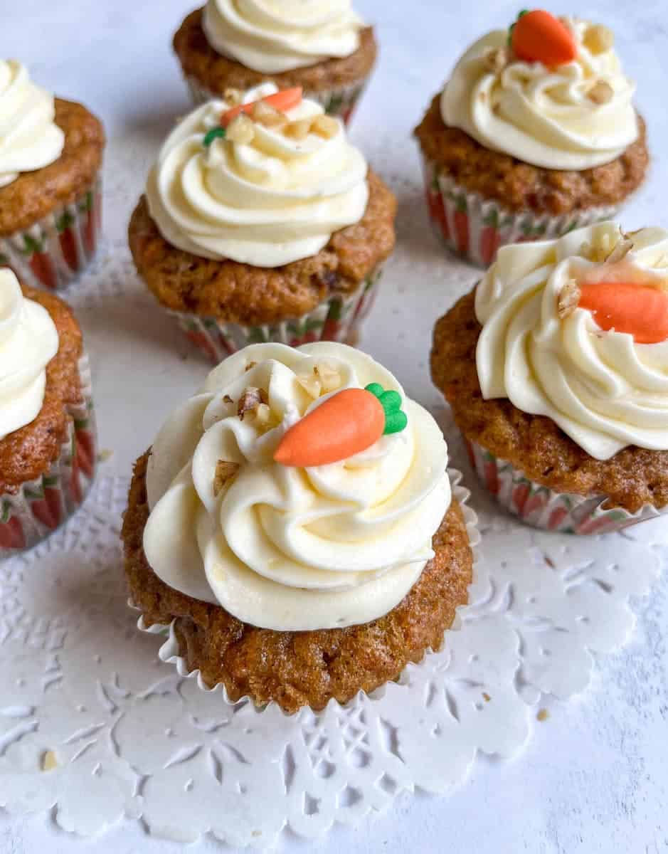 seven carrot cake cupcakes decorated with a cream cheese icing swirl, chopped walnuts and a mini fondant carrot.