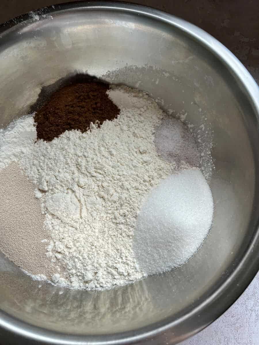 a large silver bowl of flour, mixed spice, yeast, sugar and salt.