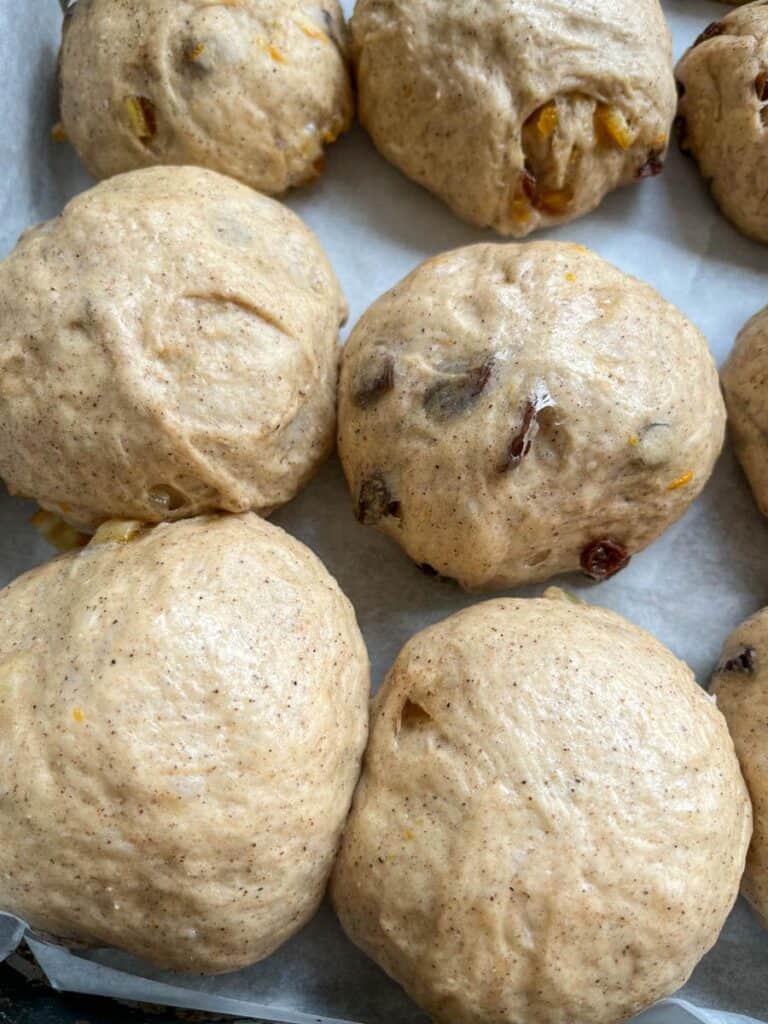 a batch of risen hot cross buns on a baking tray.