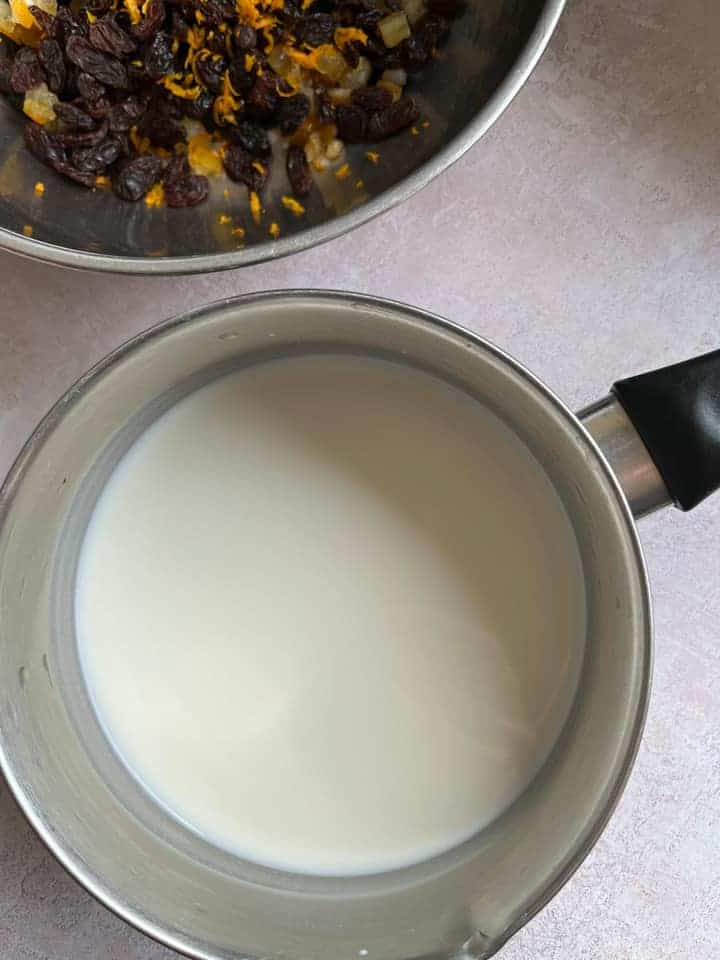 a silver saucepan of milk and a silver bowl of raisins, orange zest and mixed peel.