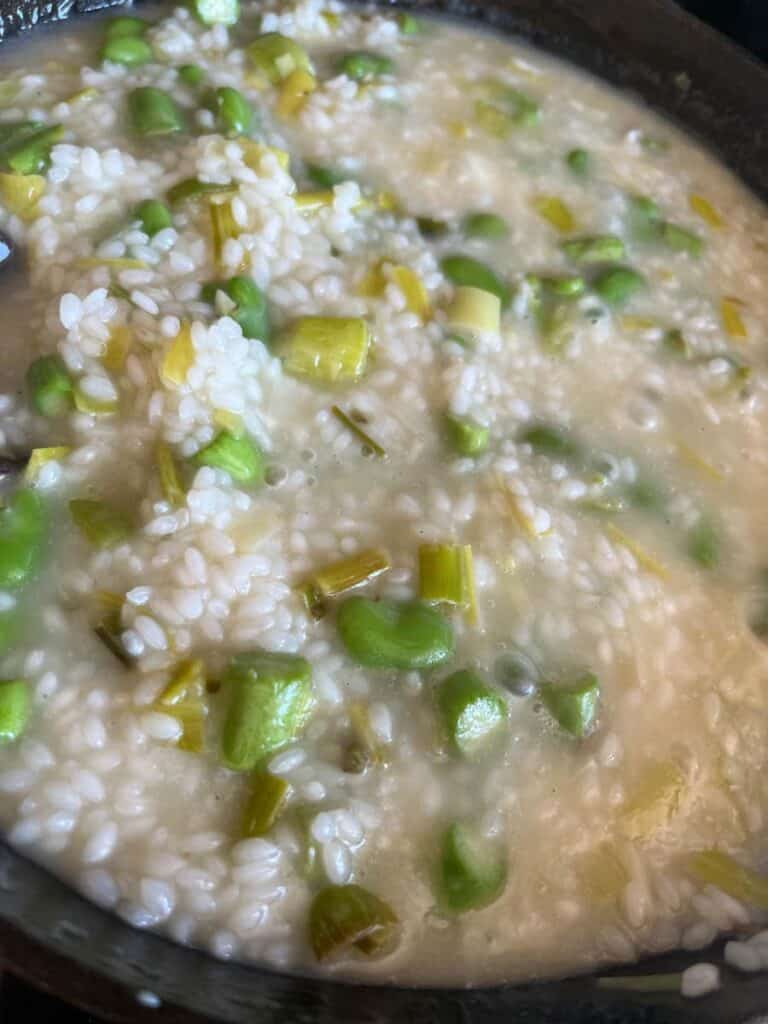 Risotto with sliced leeks and asparagus cooking in a saucepan.