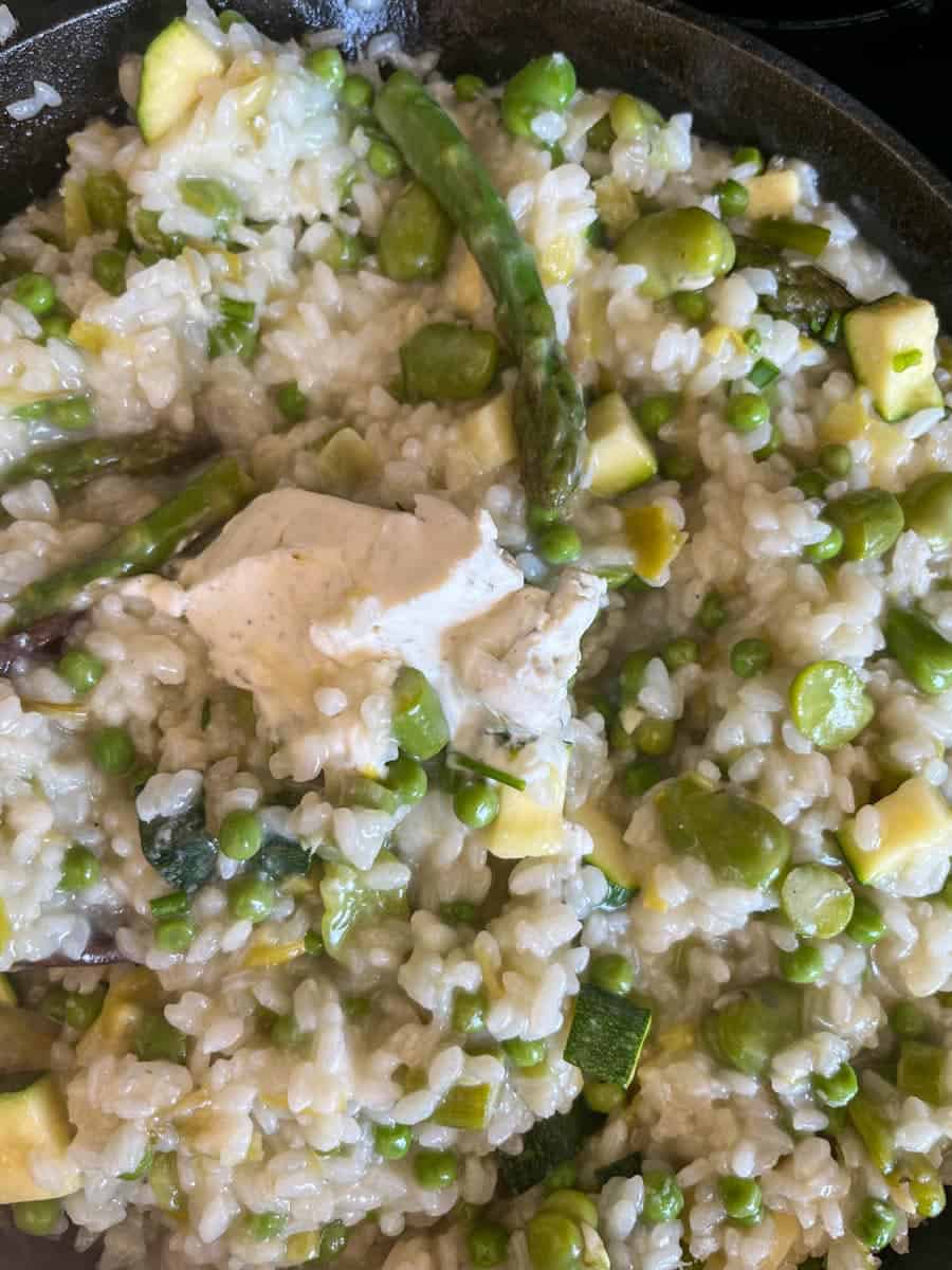 garlic and herb cream cheese being stirred into a risotto with asparagus, peas, diced courgette and broad beans.