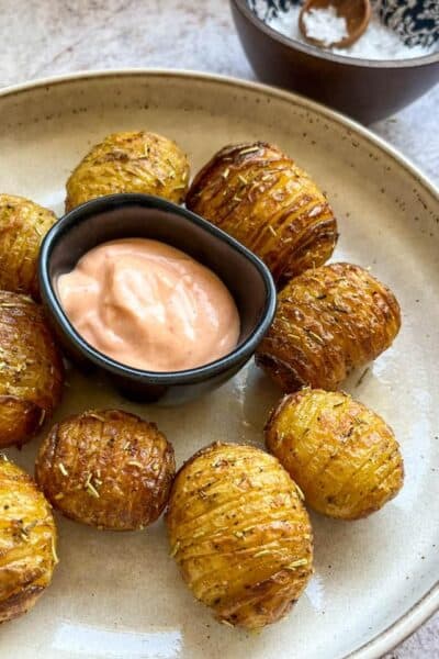 a plate of Hasselback potatoes on a beige plate with a black pot of Sriracha mayonnaise.