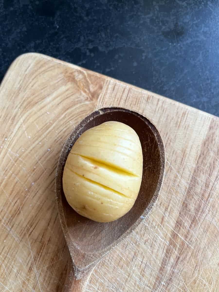 a sliced potato sitting on a wooden spoon and wooden chopping board.