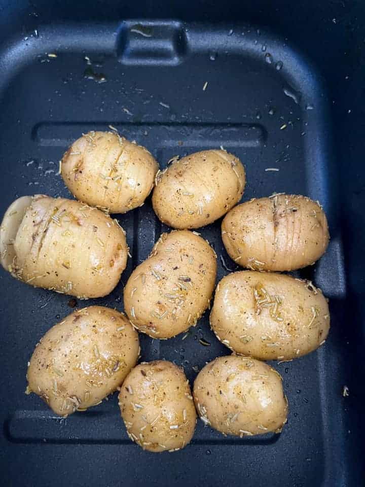 nine sliced potatoes coated in oil, salt and pepper and dried rosemary in an air fryer basket.