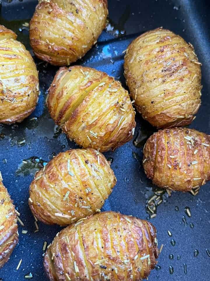 Hasselback potatoes coated in oil and dried rosemary in an air fryer basket.