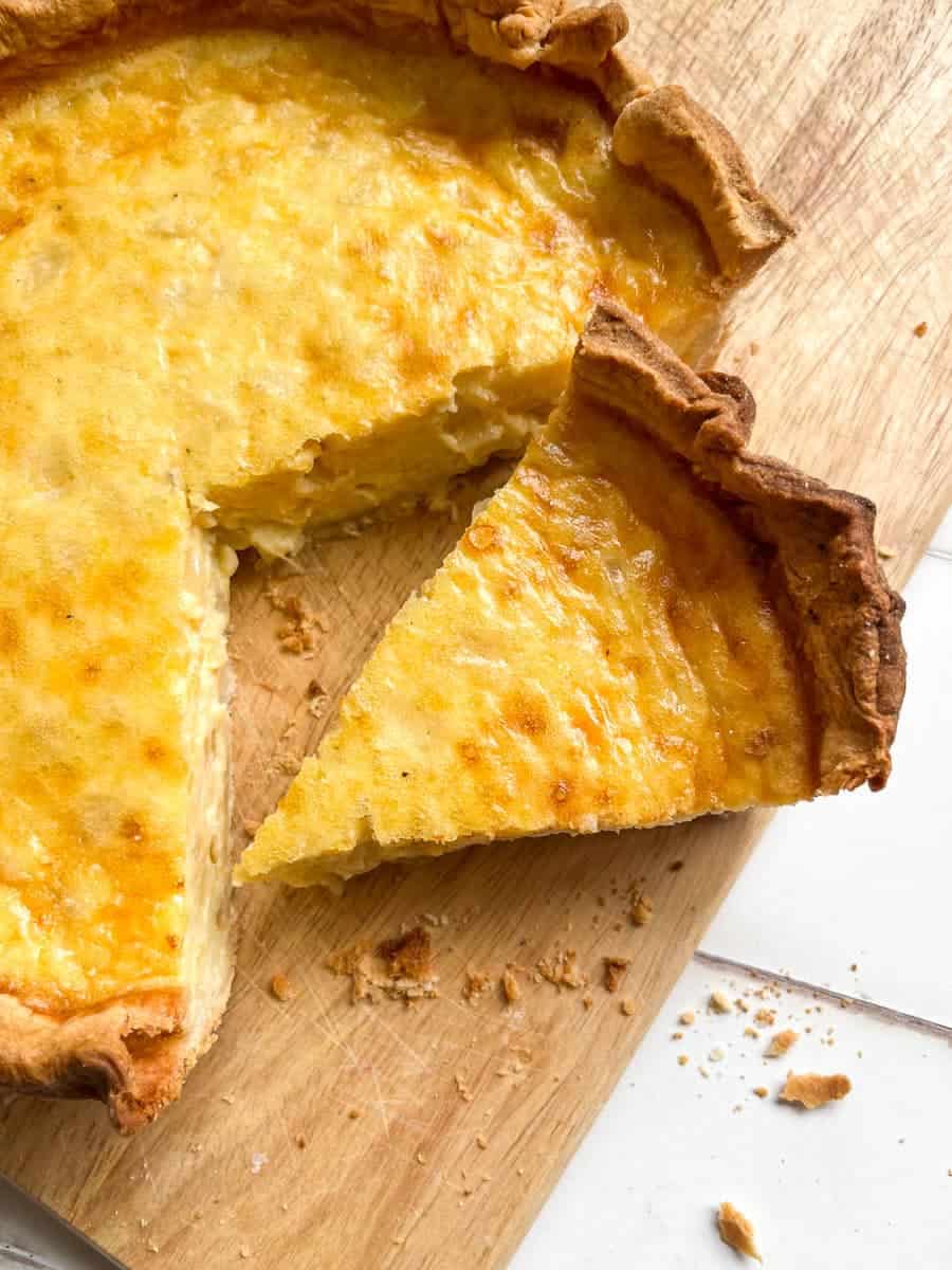 a partially sliced cheese and onion flan on a wooden chopping board.