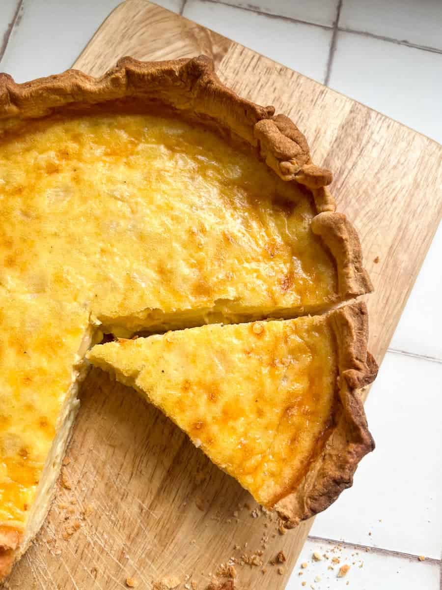 a partially sliced cheese and onion pie on a wooden chopping board.