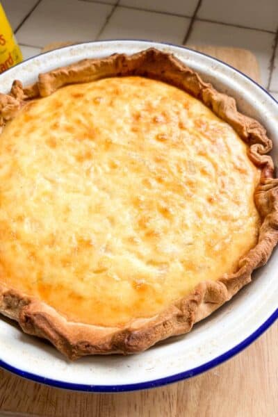 a cheese and onion pie lined with shortcrust pastry in a blue and white metal pie dish.