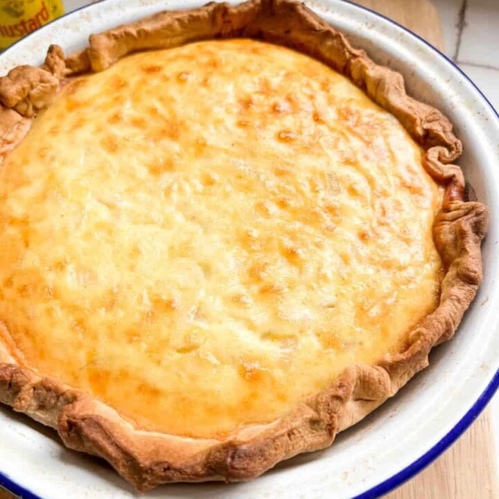 a cheese and onion pie lined with shortcrust pastry in a blue and white metal pie dish.