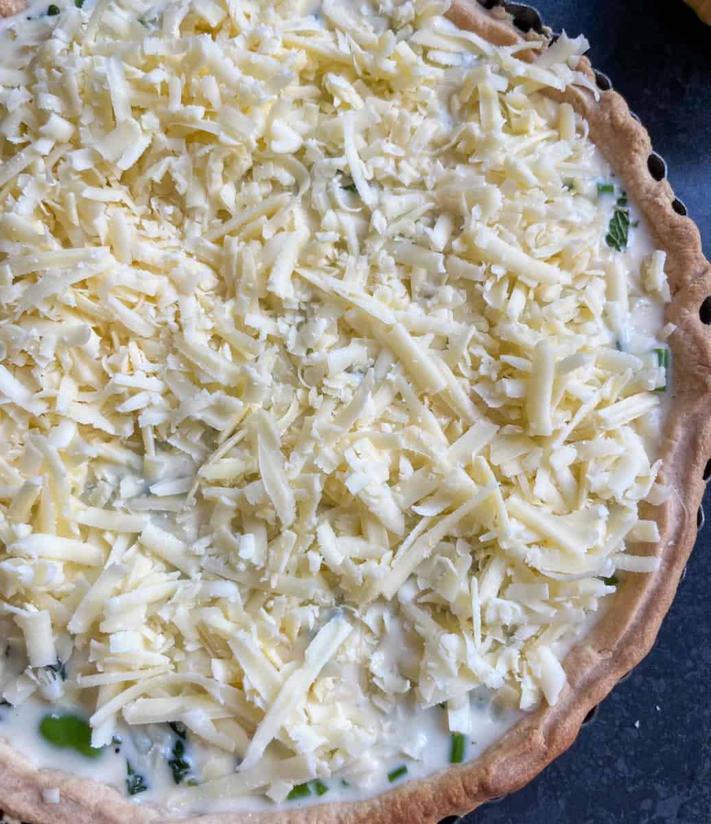 an unbaked quiche in a round tart tin sprinkled with grated cheese.