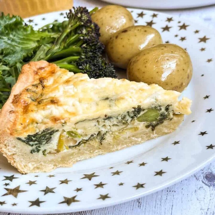 a slice of quiche with spinach, leeks and cheese, boiled potatoes and broccoli on a white and gold star plate.