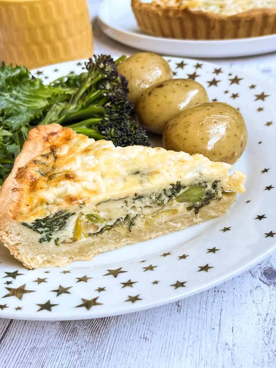 a slice of quiche with spinach, leeks and cheese, boiled potatoes and broccoli on a white and gold star plate.