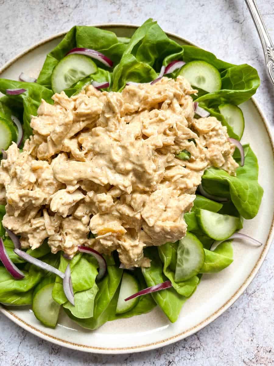 a plate of Coronation chicken on a bed of green lettuce, sliced cucumber and sliced red onion.