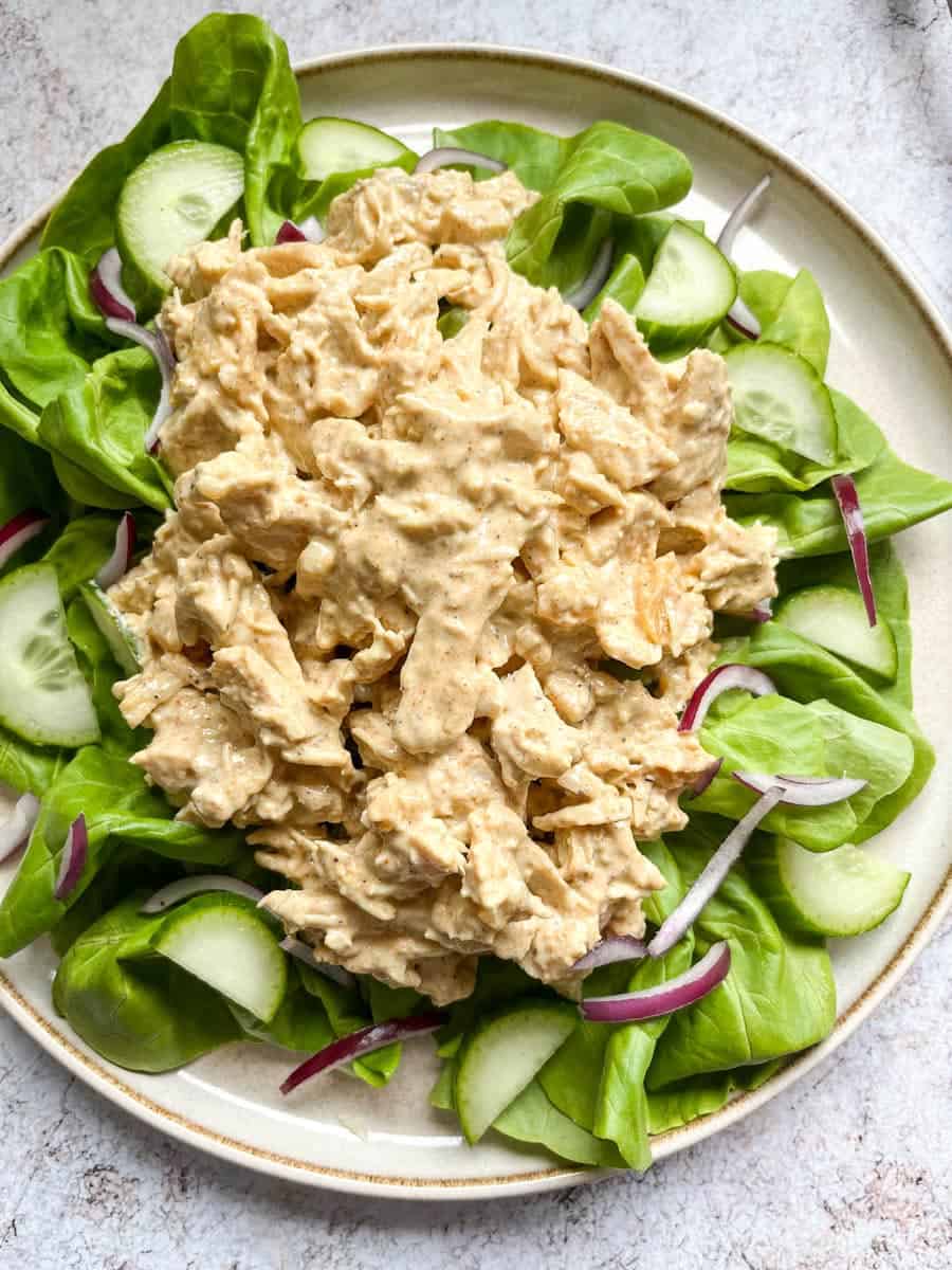 a plate of Coronation chicken on top of a bed of green lettuce, sliced cucumber and thinly sliced red onion.