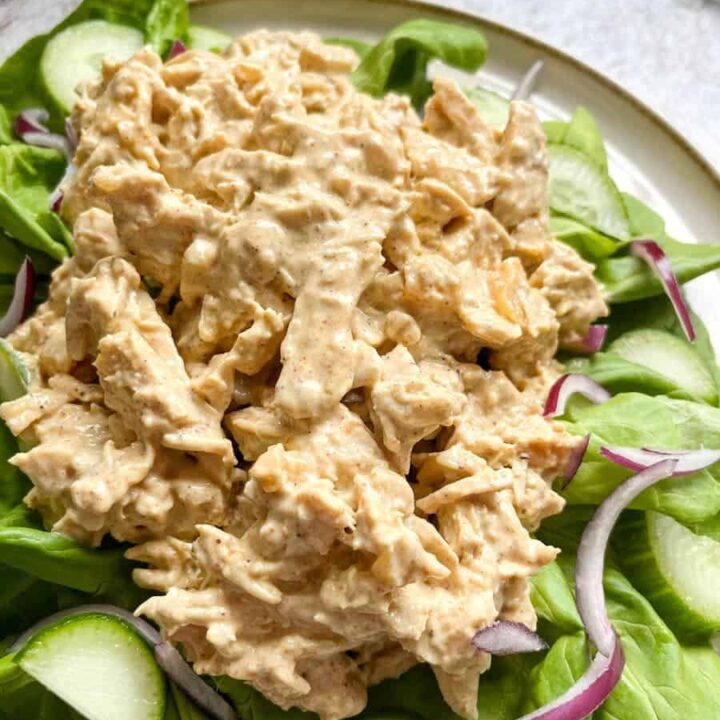 a plate of Coronation chicken on a bed of green lettuce, sliced cucumber and sliced red onion.