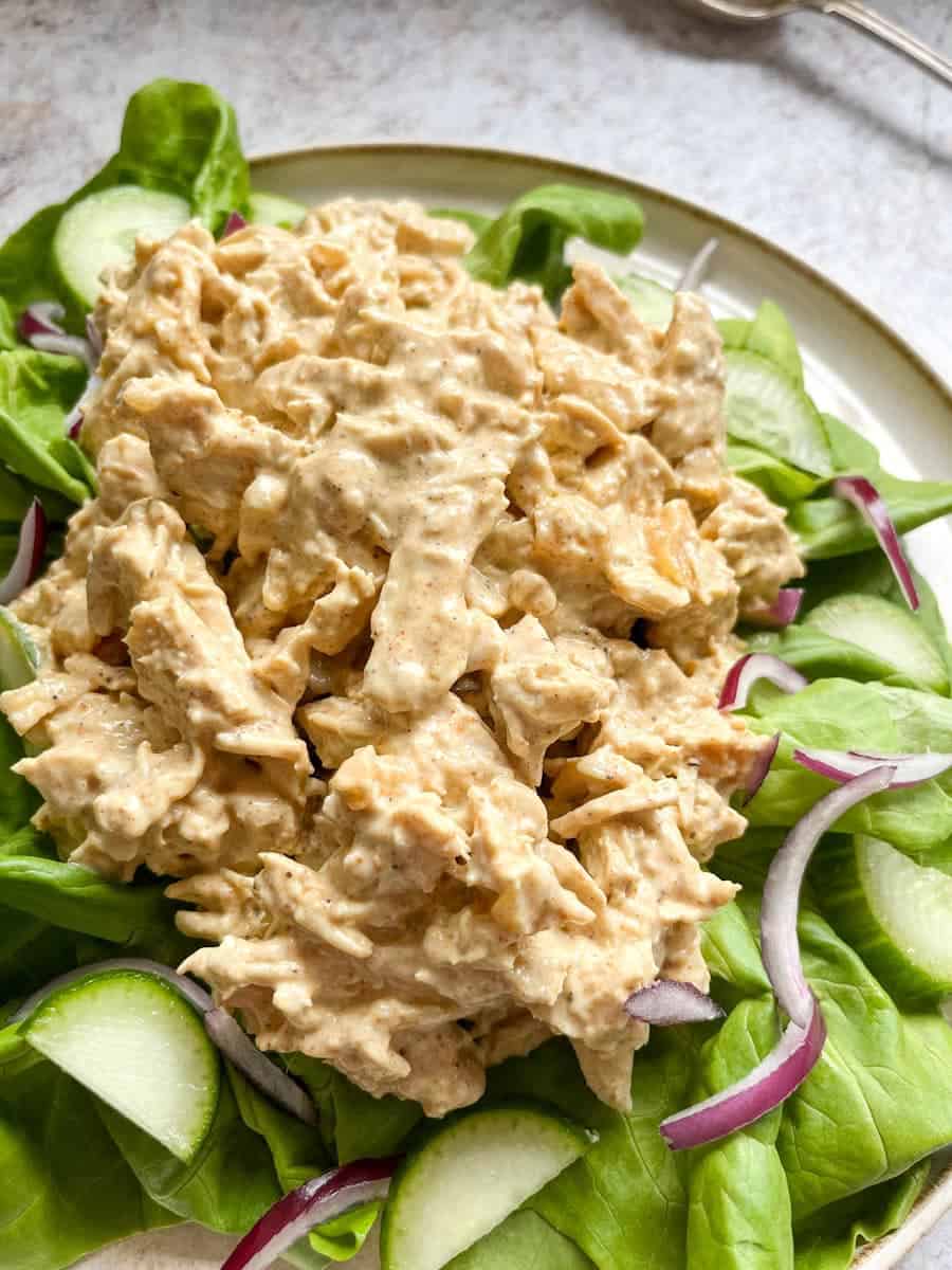 a plate of Coronation chicken on a bed of green lettuce, sliced cucumber and sliced red onion.