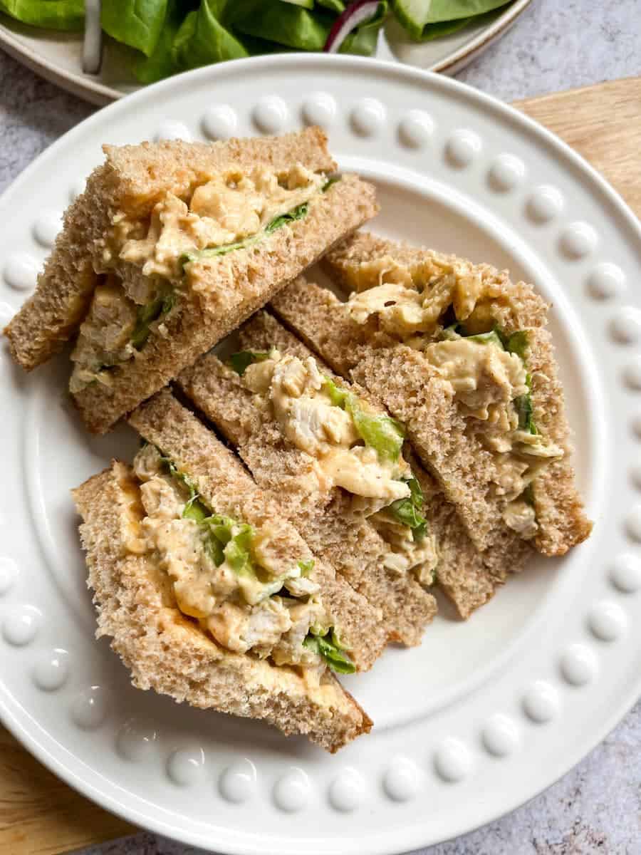A curried chicken sandwich with lettuce cut into four triangles on a white plate.