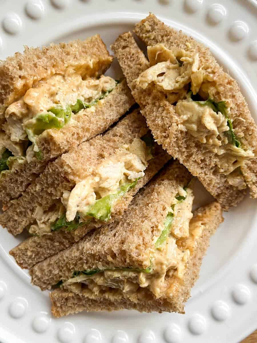 A chicken sandwich with curried mayonnaise with lettuce cut into four triangles on a white plate.