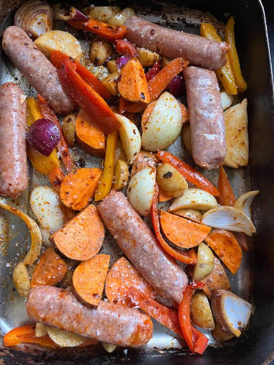 a pan of uncooked pork sausages, sliced red and yellow peppers, sliced red and white onion and sweet poatoes.
