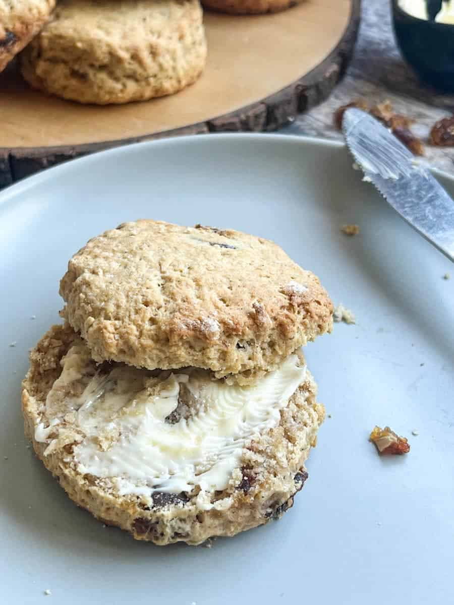 a date and walnut scone split in half and spread with butter on a grey plate with a knife.