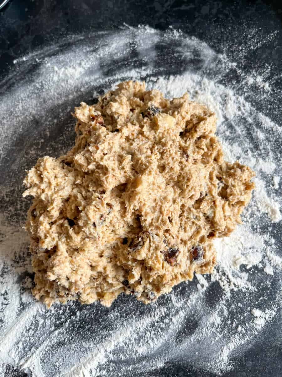 a scone mixture with dates and chopped walnuts on a dark grey kitchen worktop sprinkled with flour.