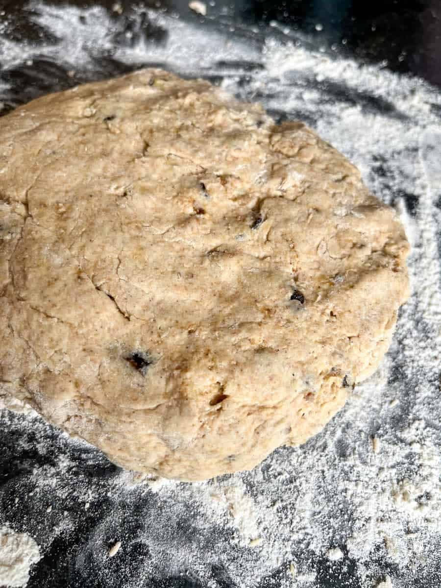a scone dough with chopped dates and walnuts on a dark grey kitchen worktop sprinkled with flour.