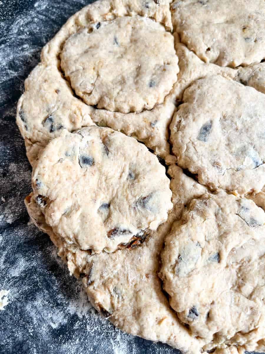 a date and walnut scone dough cut into circles on a dark grey kitchen worktop.