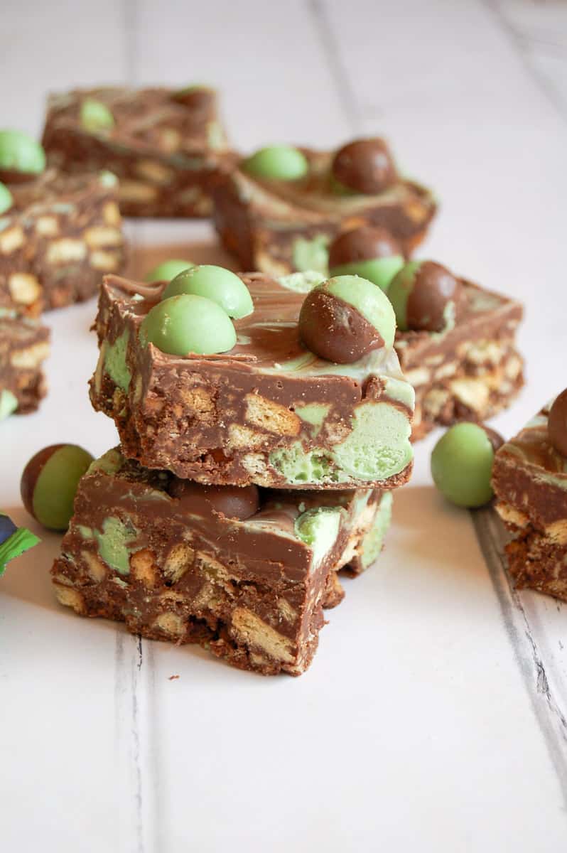 two pieces of mint Aero traybake with crushed biscuits and Aero chocolate sitting on top of each other. More squares of traybake can be seen in the background.