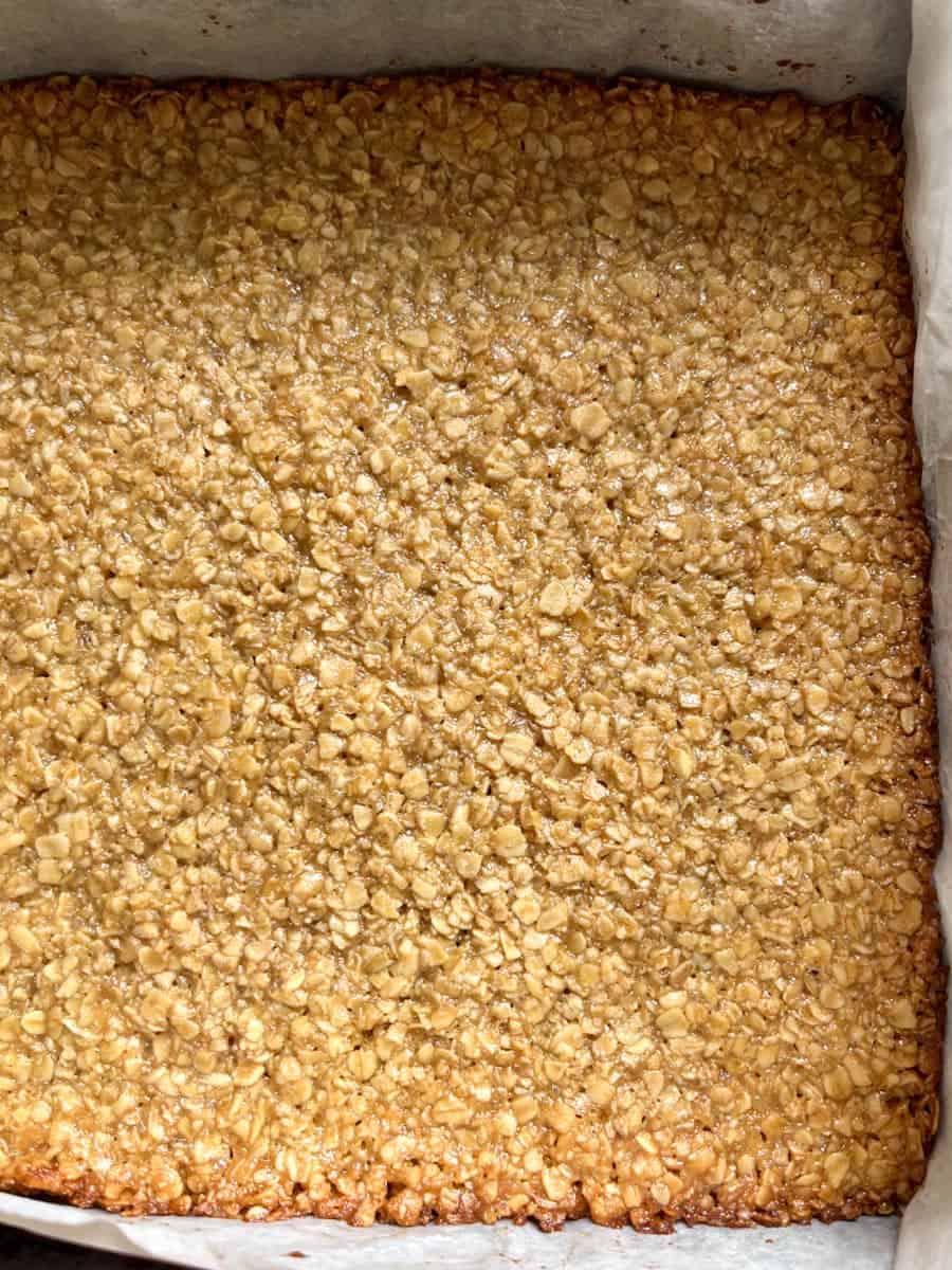 Freshly baked oat flapjack in a square tin lined with baking parchment.