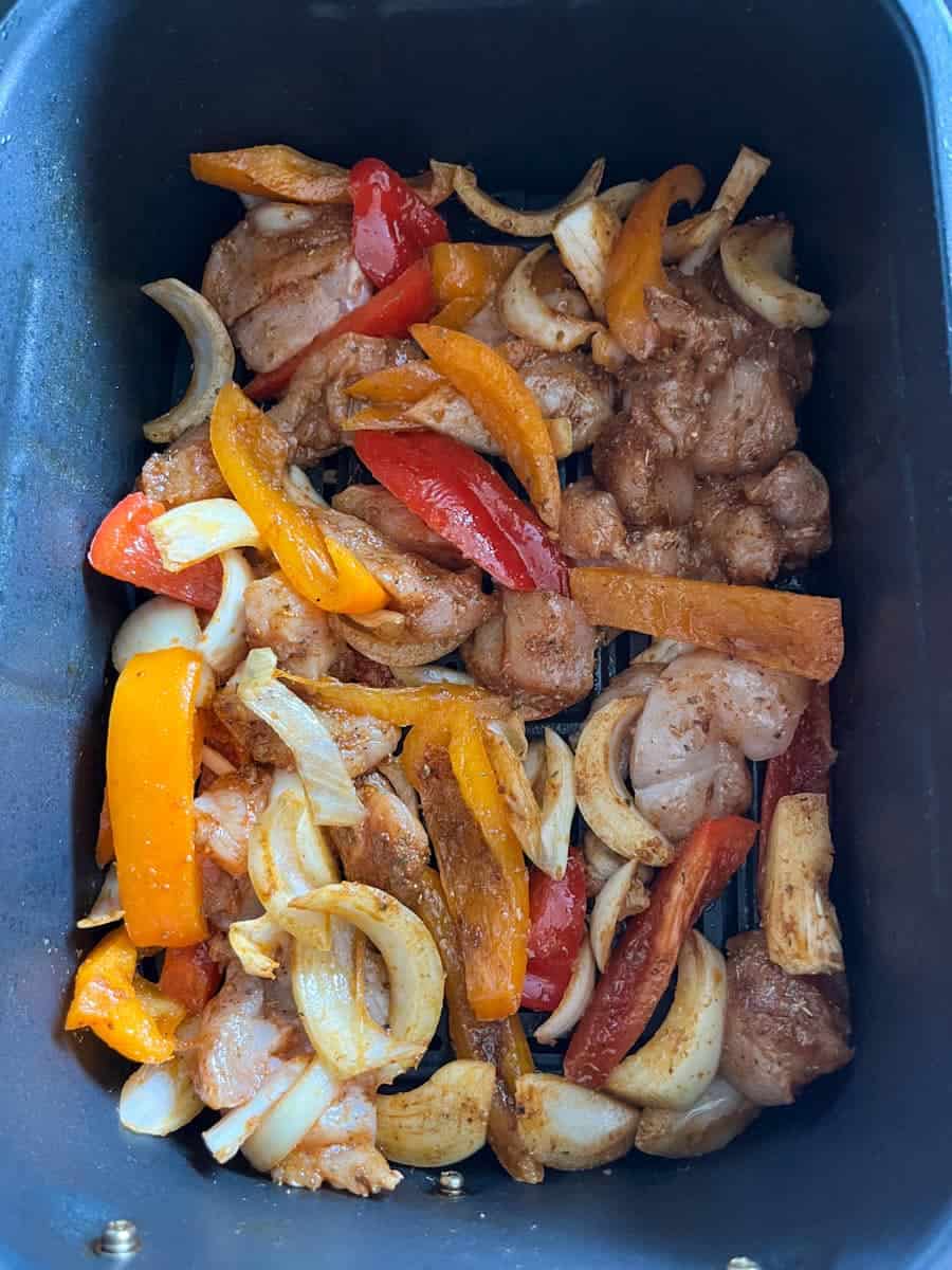 Diced uncooked chicken, onion and peppers inside an air fryer basket.