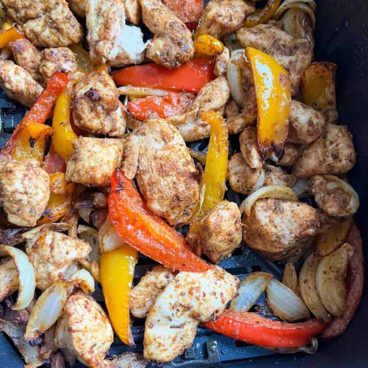 cooked chicken pieces, onions and red and yellow peppers inside an air fryer basket.