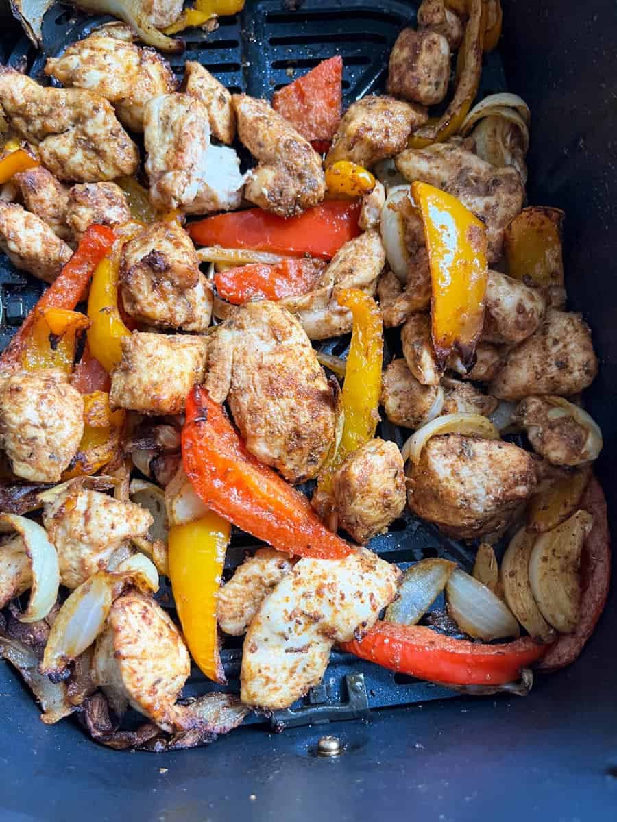 cooked chicken pieces, onions and red and yellow peppers inside an air fryer basket.