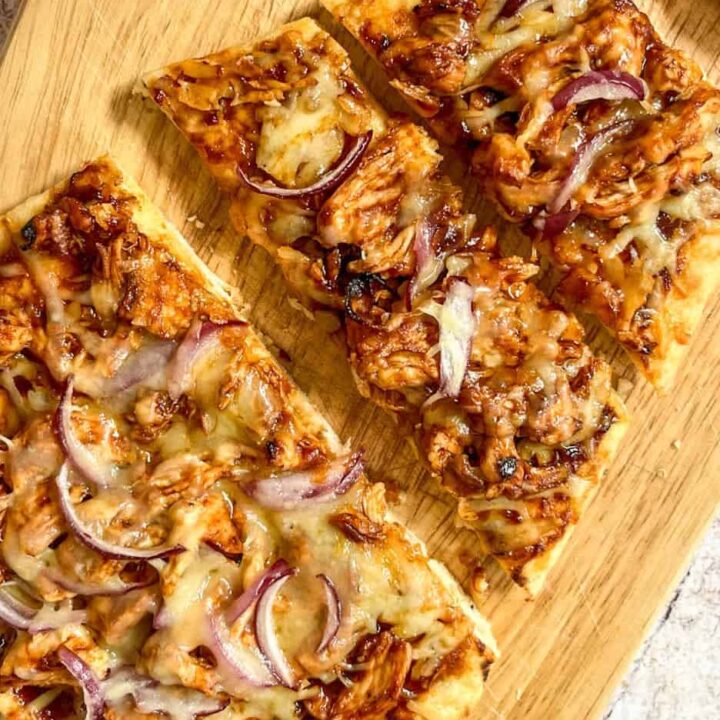a sliced Naan bread pizza with bbq sauce, chicken, sliced red onion and melted cheese.