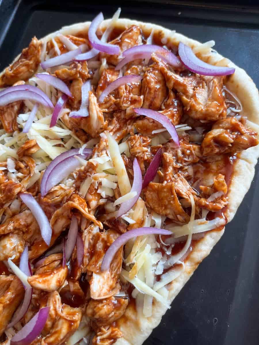an uncooked bbq chicken pizza on a baking tray.