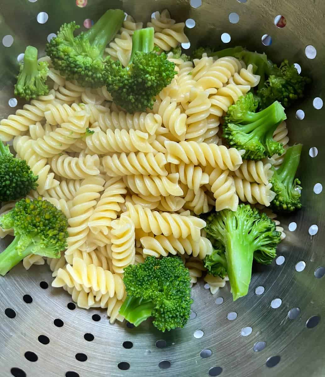 a silver colander of cooked Fusilli pasta and broccoli florets.