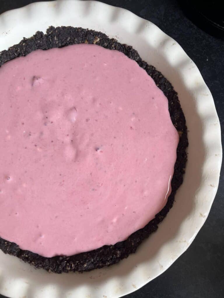 a large pie dish with a crushed chocolate cookie crust and a melted strawberry ice cream filling.