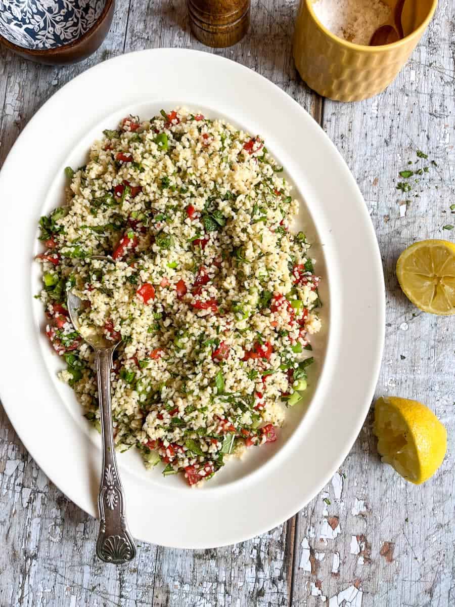 A Tabbouleh salad with diced tomatoes and fresh herbs on a white plate with a silver spoon.