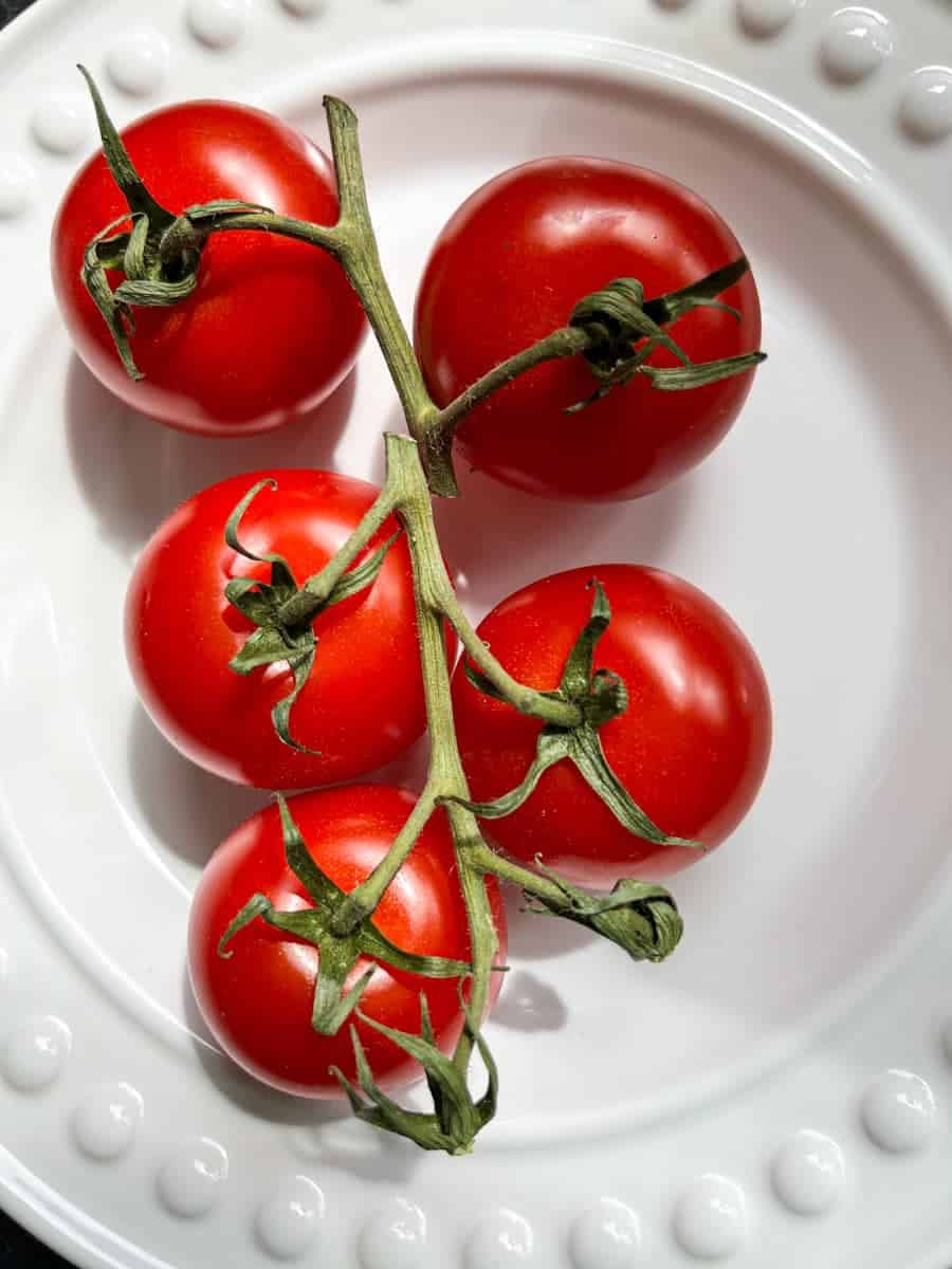 a bunch of tomatoes on the vine on a white plate.