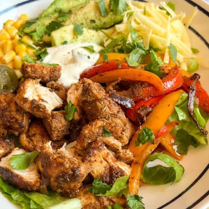 A blue and white bowl of Fajita spiced chicken chunks, onions and peppers with shredded lettuce, sweetcorn, avocado, grated cheese and sour cream.