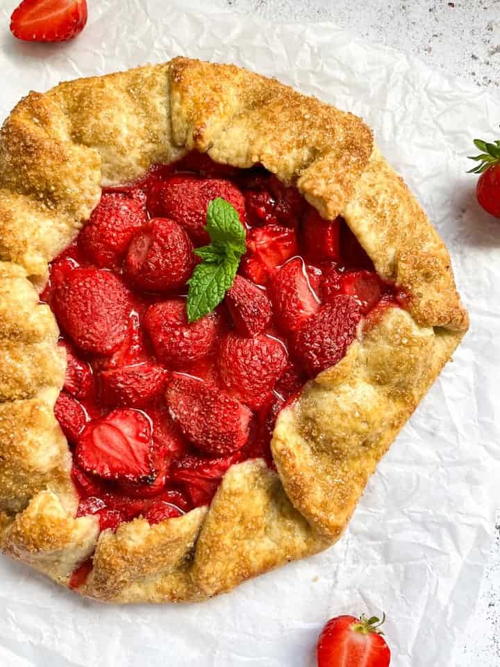 A freshly baked Galette filled with strawberries and topped with a sprig of fresh mint on a piece of baking parchment.