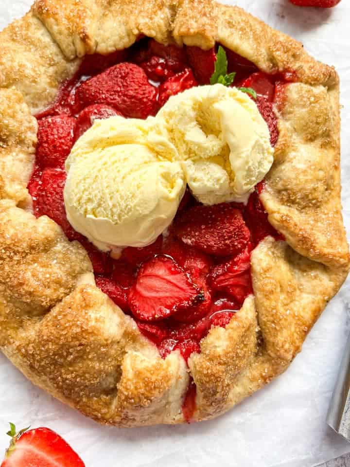 A strawberry Galette topped with two scoops of vanilla ice cream on a piece of baking parchment.